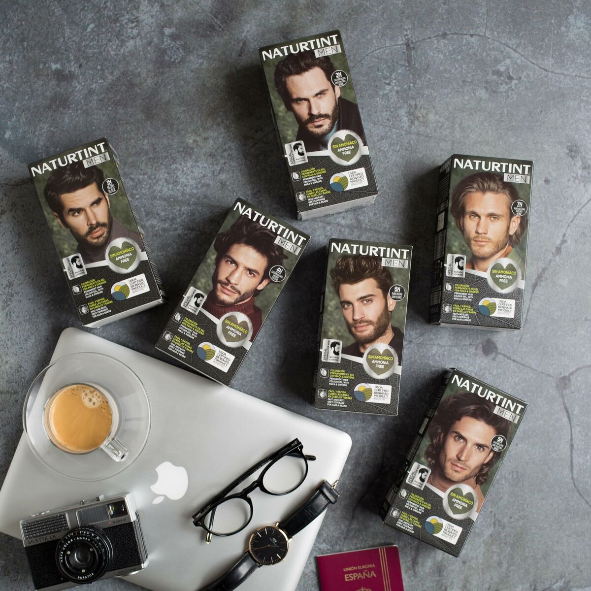 Various Naturtint Men hair dye boxes displayed on a table with coffee and camera accessories.